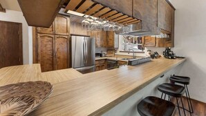 Een moderne keuken met houten kastjes, roestvrijstalen apparatuur, een lang aanrecht en hangende lampen.