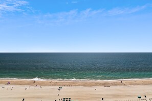 Ein Strand mit blauem Himmel, ruhigem Meer und sandigem Ufer, an dem sich Sonnenschirme und Menschen befinden.