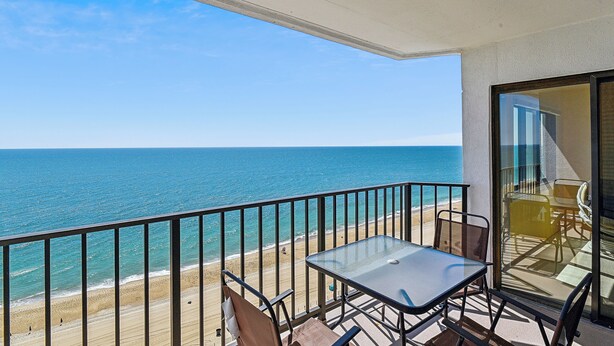 Ein Balkon mit Glastisch und Stühlen, der auf einen Strand und den Ozean blickt.
