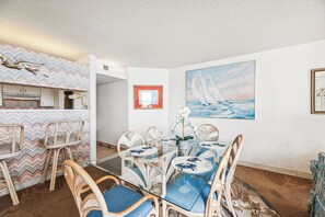 A dining area with a glass table, wicker chairs, and a patterned wall.