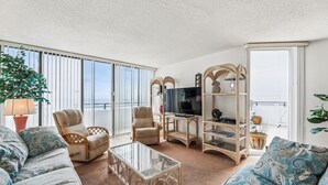 Ein Wohnzimmer mit einer Couch, Sesseln, einem Glastisch und einem Fernseher.