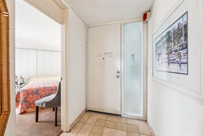 Habitación de hotel con una cama, una silla, una puerta con un panel de vidrio esmerilado y un cuadro enmarcado en la pared.