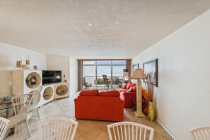 A modern living room with a red sofa, a flat-screen TV, and a dining area with white chairs.