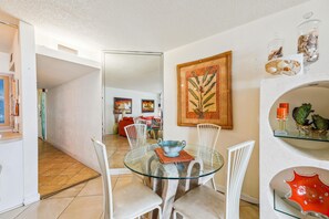 A dining area with a glass table, white chairs, and a red sofa in the background.