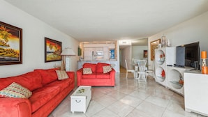A living room with red sofas, a white coffee table, and a kitchen in the background. - Includes Xplorie Activities and Linens. PYRAMID - 2BR oceanfront condo w/outdoor pool. (Ocean City)