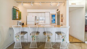 A kitchen with white cabinets, a microwave, a stove, and a bar area with four white chairs. - Includes Xplorie Activities and Linens. PYRAMID - 2BR oceanfront condo w/outdoor pool. (Ocean City)