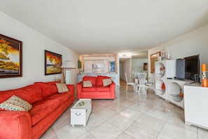 A modern living room with red sofas, a white coffee table, and a kitchen in the background. - Includes Xplorie Activities and Linens. PYRAMID - 2BR oceanfront condo w/outdoor pool. (Ocean City)