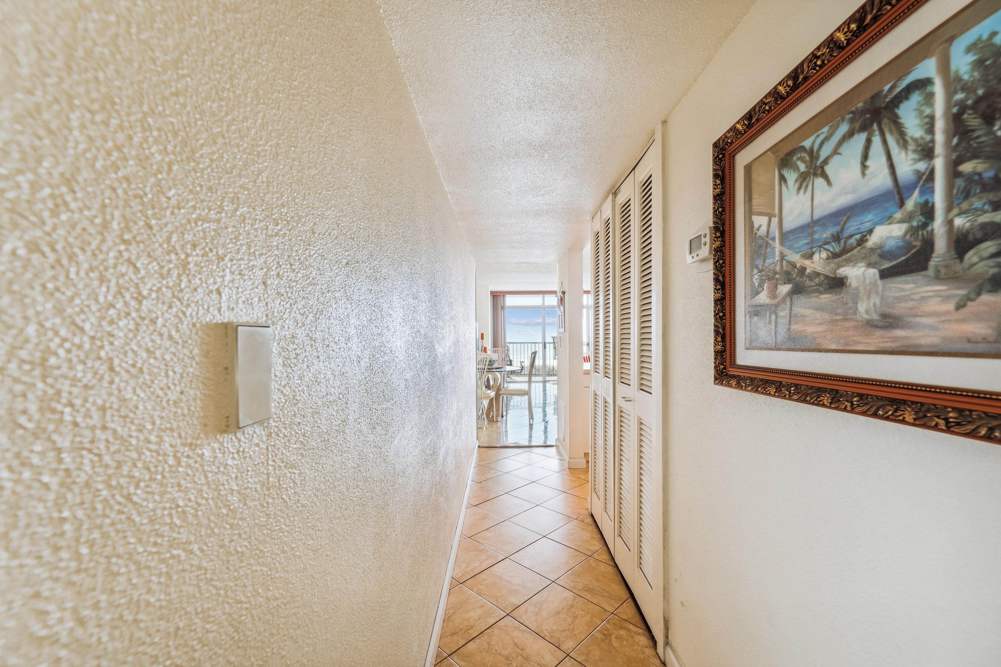 Un couloir avec un sol carrelé, un tableau accroché au mur et une porte donnant sur un balcon.