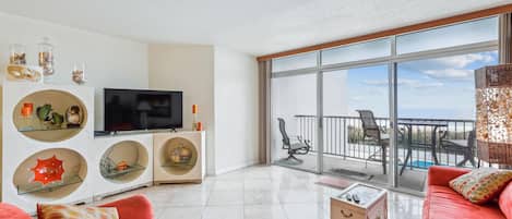 A modern living room with a flat-screen TV, red sofas, decorative shelves, and a balcony with outdoor furniture.