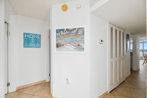 A hallway with a door on the left, a framed picture on the wall, and a thermostat on the right.
