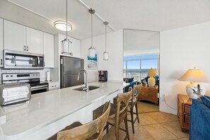 Een moderne keuken met roestvrijstalen apparatuur, een groot kookeiland met barkrukken en uitzicht op de oceaan door een groot raam.