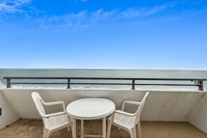 A balcony with a white table and two chairs, overlooking a beach with waves.