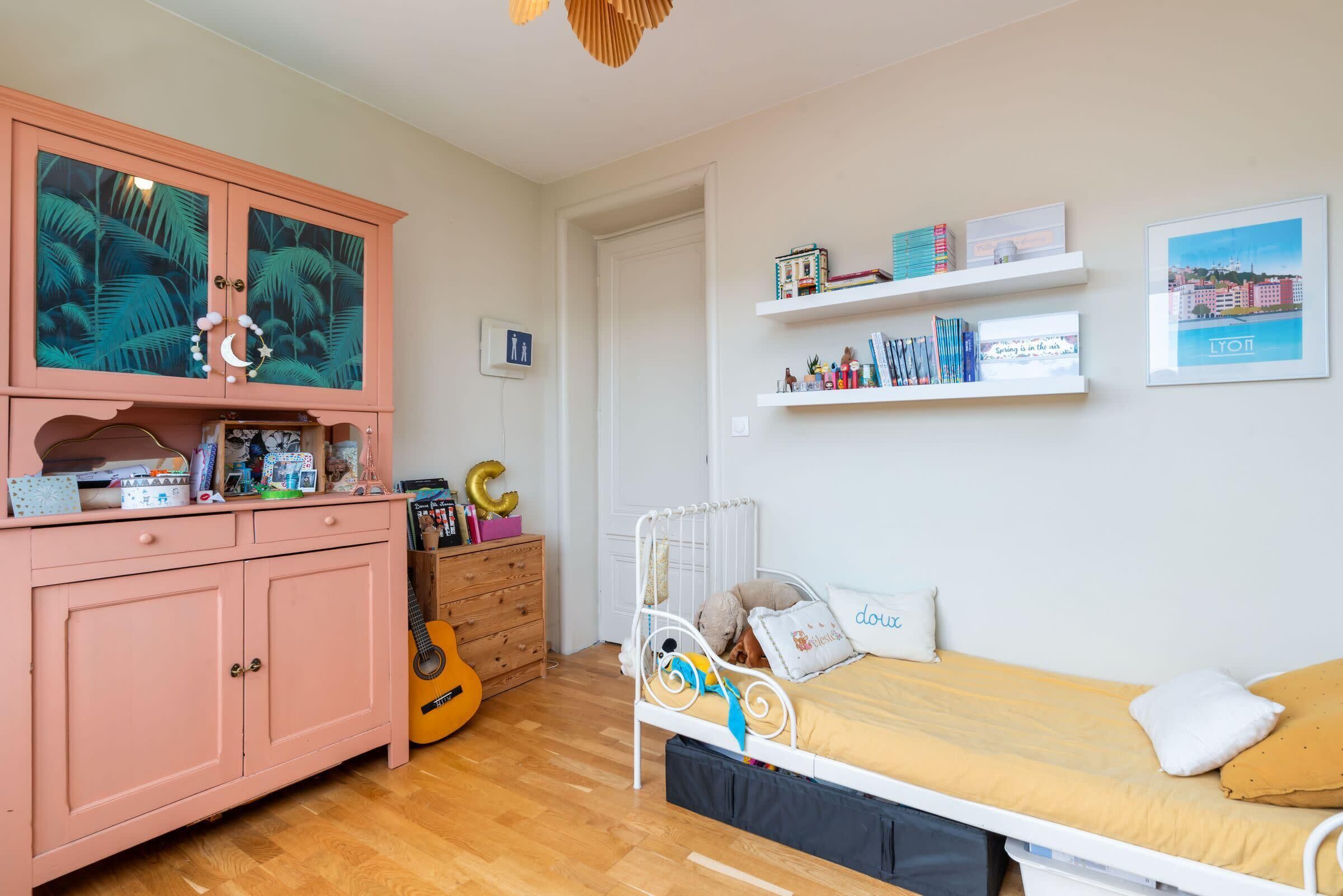 Ein Schlafzimmer mit einem Bett, einem rosa Schrank, einer Gitarre und einem Regal mit Büchern und einem gerahmten Bild.