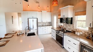 Una cocina amplia con armarios blancos, una isla grande e iluminación colgante.
