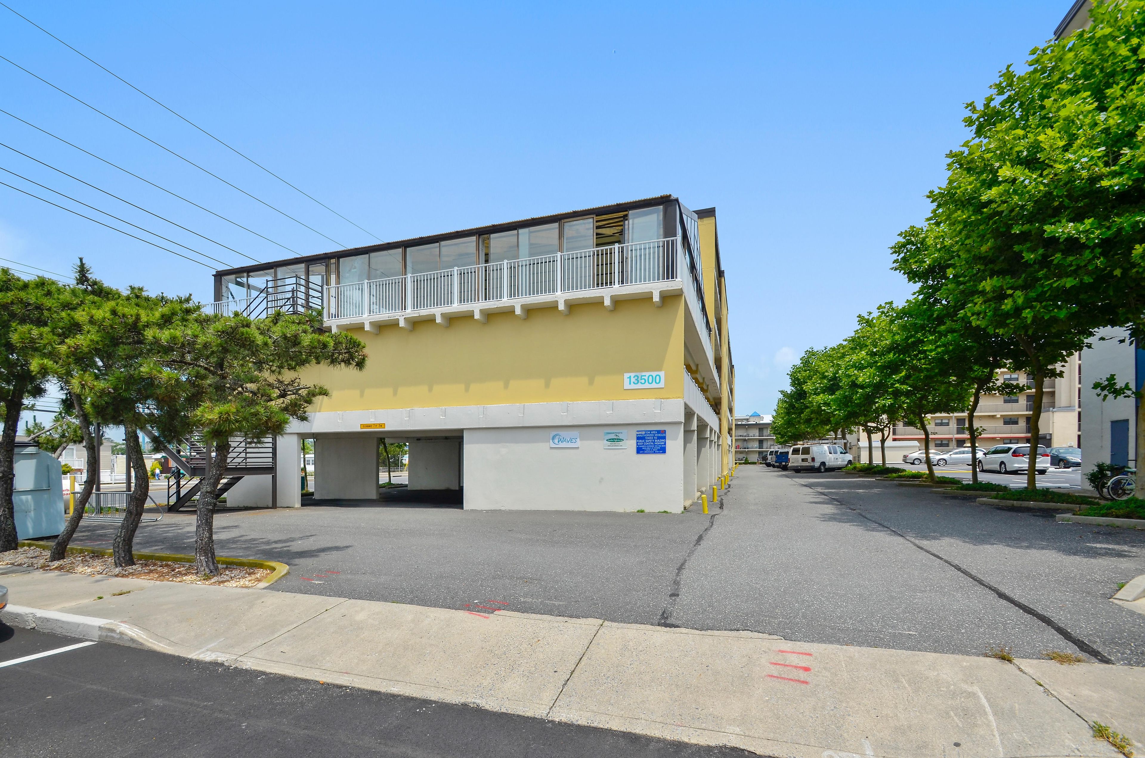 A multi-story building with a yellow facade, a covered parking area, and a clear sky.