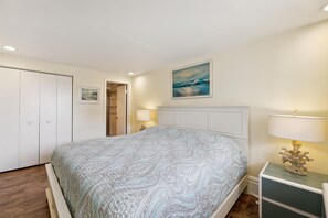 Une chambre à coucher avec un lit, une table de chevet, une lampe, un tableau et une porte.