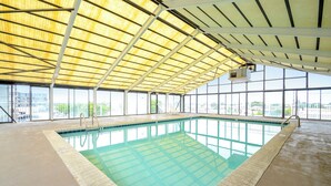Ein Hallenbad mit klaren Glaswänden, einem gefliesten Boden und einer Metall-Dachkonstruktion.