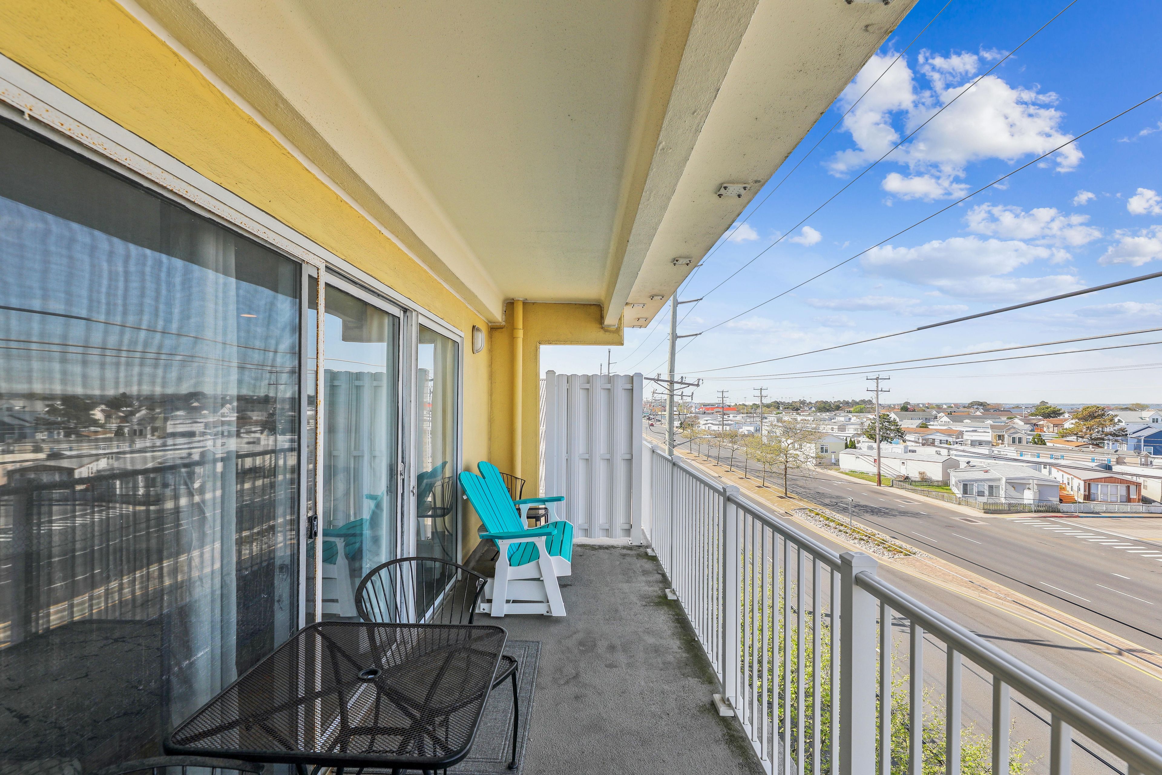 A balcony with a view of a residential area, a metal chair, and a table.