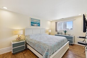 Un dormitorio con cama, mesitas de noche, un cuadro, una ventana y un televisor.