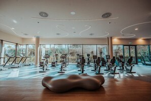 Une salle de sport moderne dotée de divers équipements d’exercice, de grandes fenêtres et d’un design de plafond original.