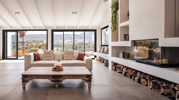 A spacious living room with a large window, a beige sofa, a wooden coffee table, and a fireplace. - Villa Jade (La Mandarina)