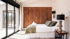 A bedroom with a large bed, wooden headboard, two bedside lamps, and a view through a glass door. - Villa Jade (La Mandarina)