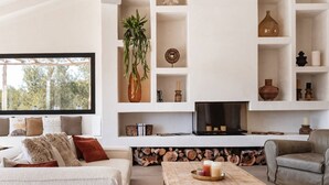 A modern living room with a sofa, coffee table, and TV. There are shelves with decorative items and a window with a view of trees. - Villa Jade (La Mandarina)