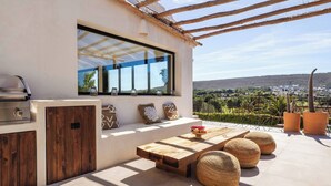 An outdoor patio with a wooden table, seating, and a grill. - Villa Jade (La Mandarina)