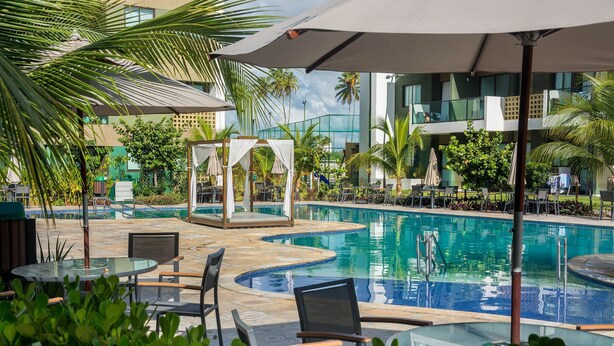 Un área de piscina con sillones de playa, sombrillas y una cabaña.