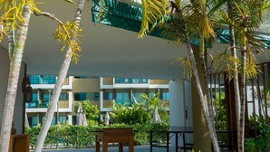 Un patio de hotel con palmeras, un banco de madera y una zona de piscina.