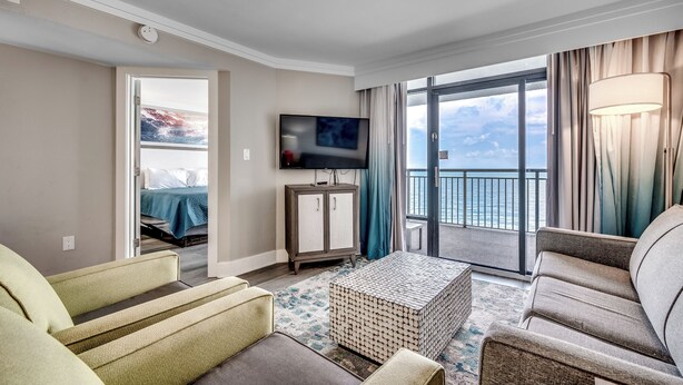 Een moderne hotelkamer met een balkon, een flatscreen televisie en een zithoek met een gestreept voetenbankje.
