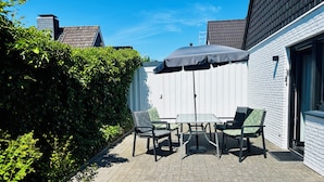 A patio with a table and chairs, a covered umbrella, and a white brick wall.