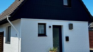 A single-story house with a black roof, white exterior walls, a small window, and a door.