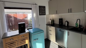 A compact kitchen with a built-in dishwasher, a small fridge, and a window with curtains.