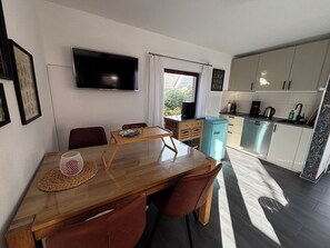 A compact living space with a dining area, kitchenette, and a TV mounted on the wall.