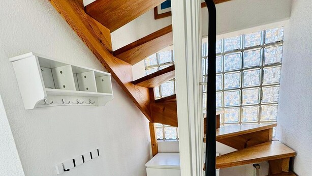 A modern staircase with wooden steps and a white wall with a built-in shelf.