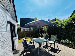 A patio with a table and chairs, a covered umbrella, and a white brick wall.