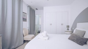 A modern hotel room with a large bed, a chair, a wardrobe, and a small table with a lamp. - Spacious cozy 2BR/2BA in the city center (Gibraltar)