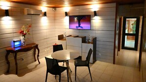 Una cocina moderna con comedor, que presenta un techo de madera, paredes de azulejos blancos, un televisor de pantalla plana y un jarrón con flores sobre una mesa de madera.