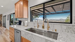 A kitchen with marble countertops, a large window with a view, and wooden cabinets. - When in Glen | Panoramic View | Pool / Hot Tub (Glen Ellen)
