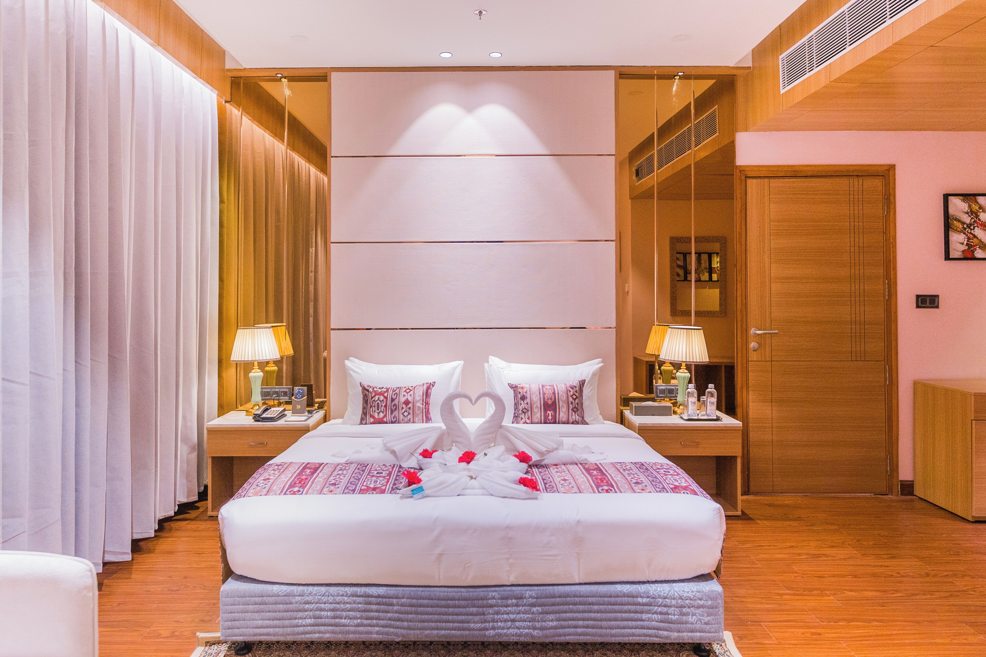 A hotel room with a large bed, two bedside tables with lamps, a wardrobe, and a door.