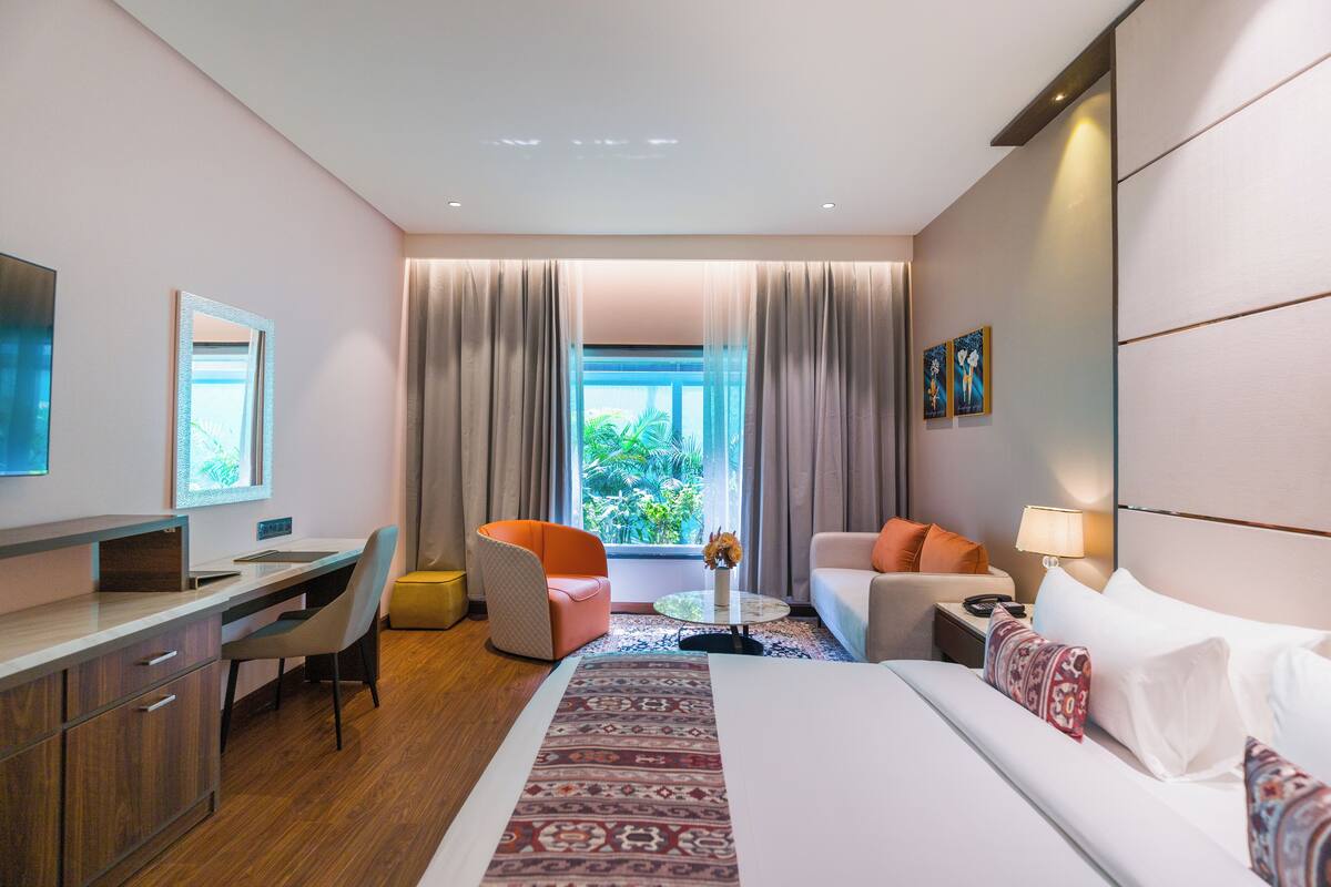 Ein Hotelzimmer mit Bett, Schreibtisch, Stuhl und Blick auf Grünflächen.