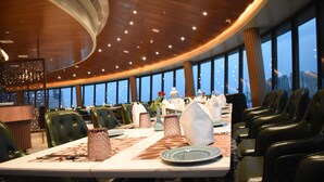 A dining area with a long table set for a meal, surrounded by chairs, and large windows offering a view of the cityscape.