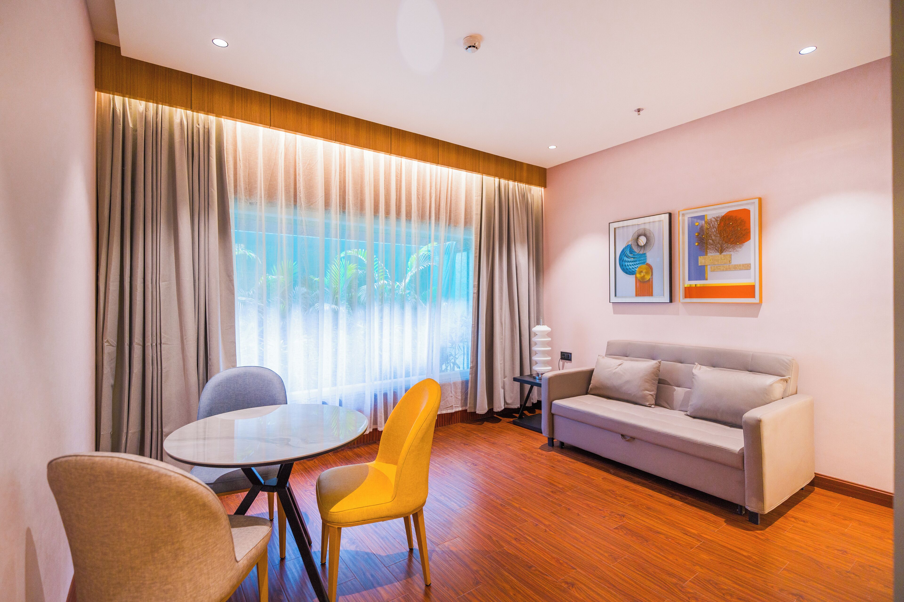 A modern living room with a sofa, a dining table with chairs, and a large window with curtains.