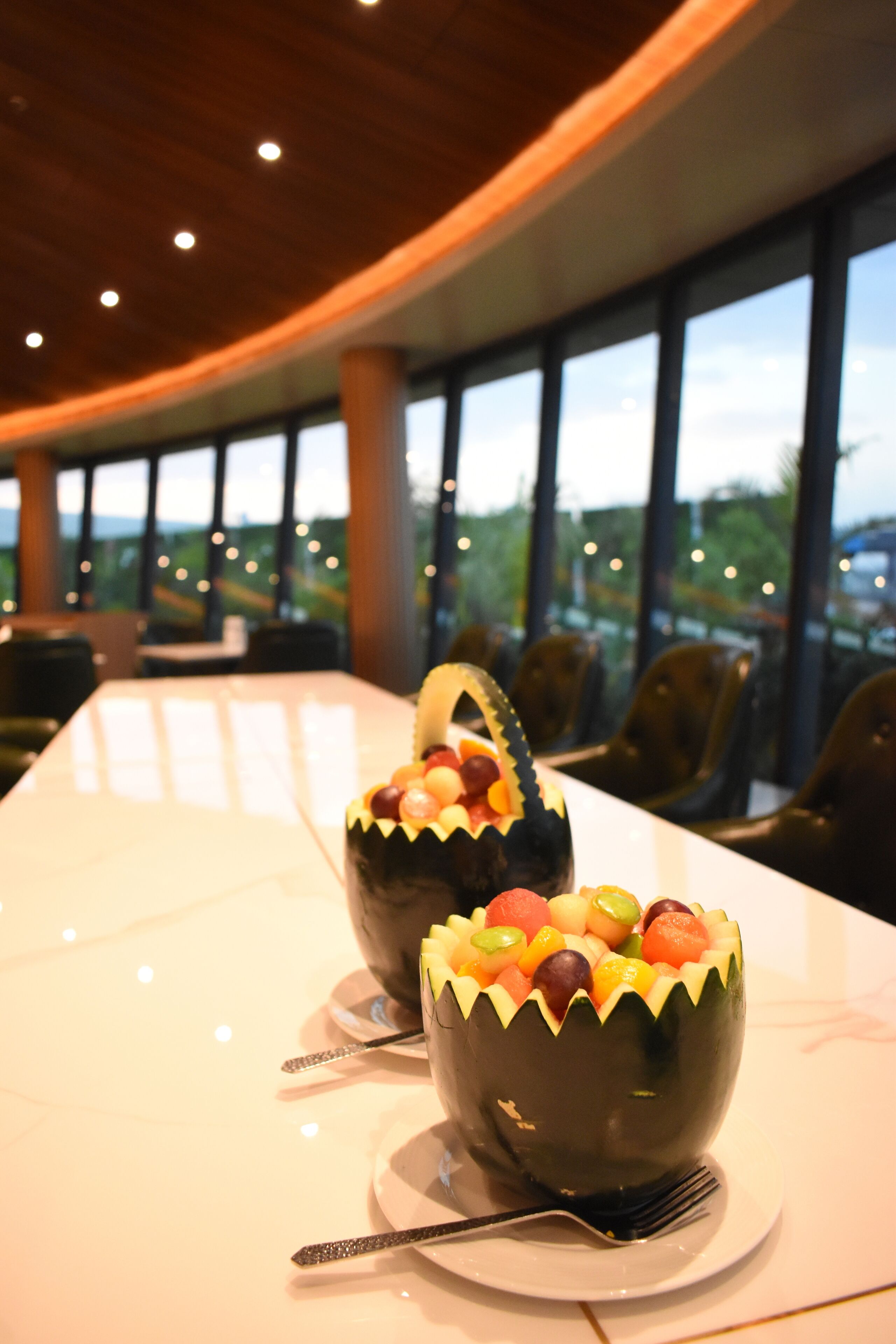 A conference table with two fruit bowls in the center, surrounded by chairs, in a room with large windows and a curved ceiling.