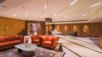 A spacious lobby with a modern design, featuring a seating area with orange sofas, a marble coffee table, and a patterned rug.