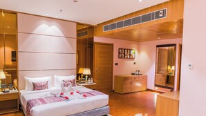 A hotel room with a large bed, bedside tables, a wardrobe, a mirror, and a small desk with a lamp.