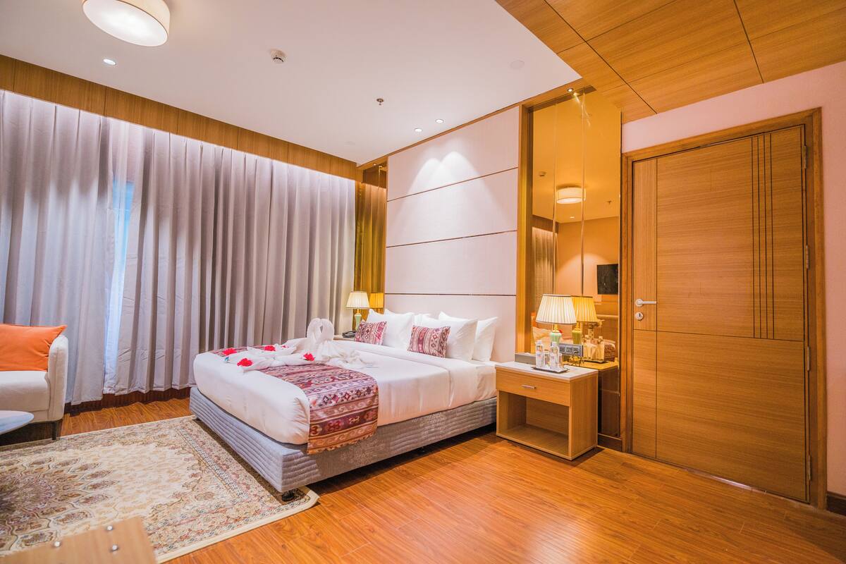 Ein Hotelzimmer mit einem großen Bett, Nachttischen, einem Holzschrank und einer Sitzecke mit einem Sessel und einem kleinen Tisch.