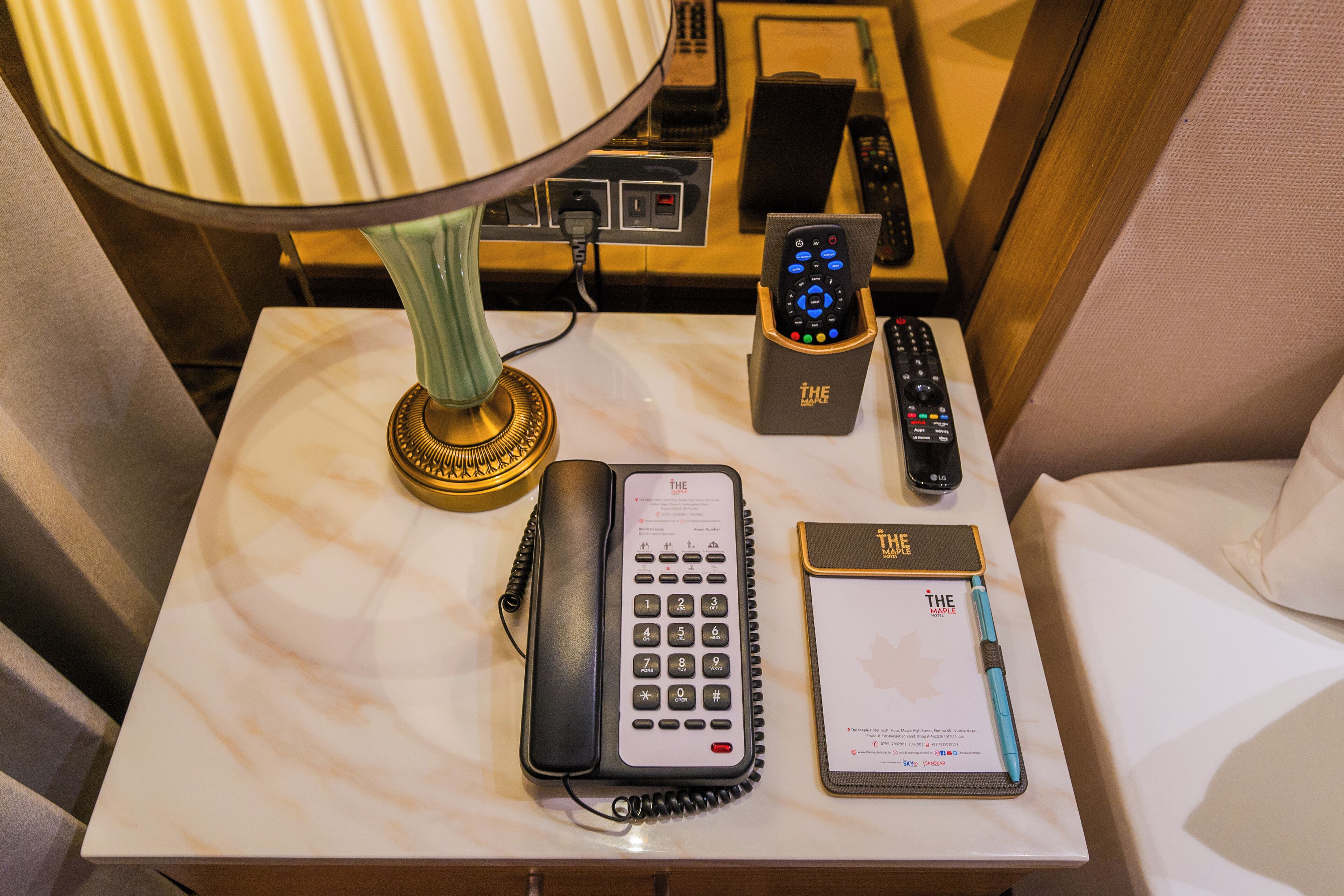 A hotel room with a marble bedside table, a telephone, a remote control, a pen, and a notepad.