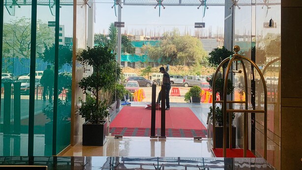 A hotel lobby with a red carpet, glass walls, and a chandelier.